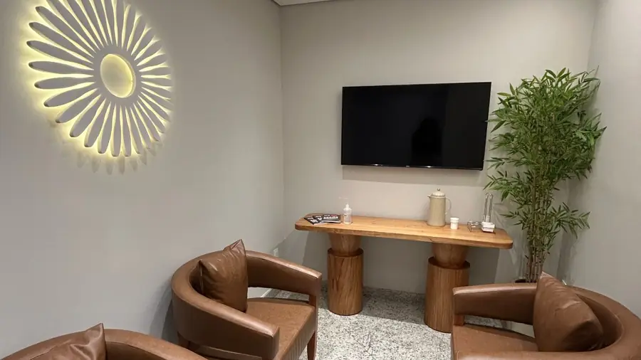 Sala de espera da Clínica de Olhos Dornelas, com poltronas de couro, televisão e o símbolo da clínica iluminado na parede.